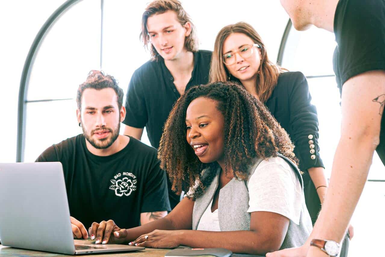 the 6 Best Professional Development Resources for Association Pros Zzeem Zzeem a Diverse Group of Five Coworkers Gathered Around a Laptop, Collaborating and Looking at the Screen in a Bright Workspace.